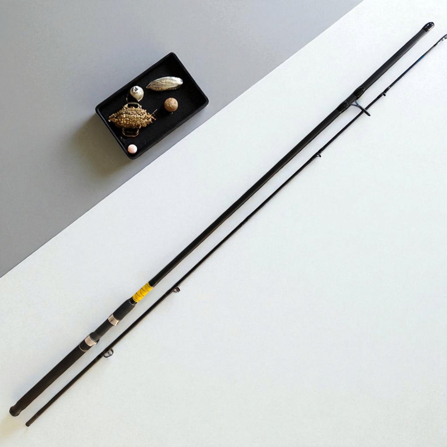 BlackFin Xtreme 9ft Premium Carbon Spinning Rod โ Two-piece ultra-lightweight fishing rod with ergonomic handle, stainless steel guides, and modern design, placed beside a tray of fishing lures on a minimalist background