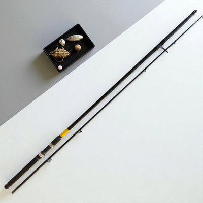 BlackFin Xtreme 9ft Premium Carbon Spinning Rod – Two-piece ultra-lightweight fishing rod with ergonomic handle, stainless steel guides, and modern design, placed beside a tray of fishing lures on a minimalist background