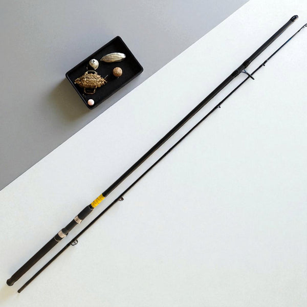 BlackFin Xtreme 9ft Premium Carbon Spinning Rod – Two-piece ultra-lightweight fishing rod with ergonomic handle, stainless steel guides, and modern design, placed beside a tray of fishing lures on a minimalist background