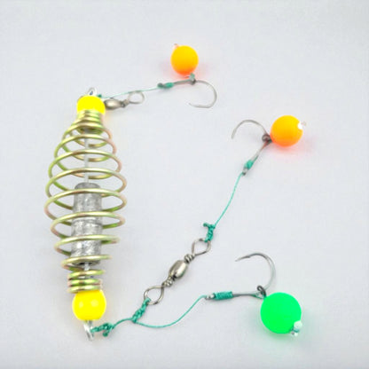 Carp fishing spring feeder rig featuring a metal coil feeder and three baited hooks tied with green fishing line, designed for groundbait fishing.
